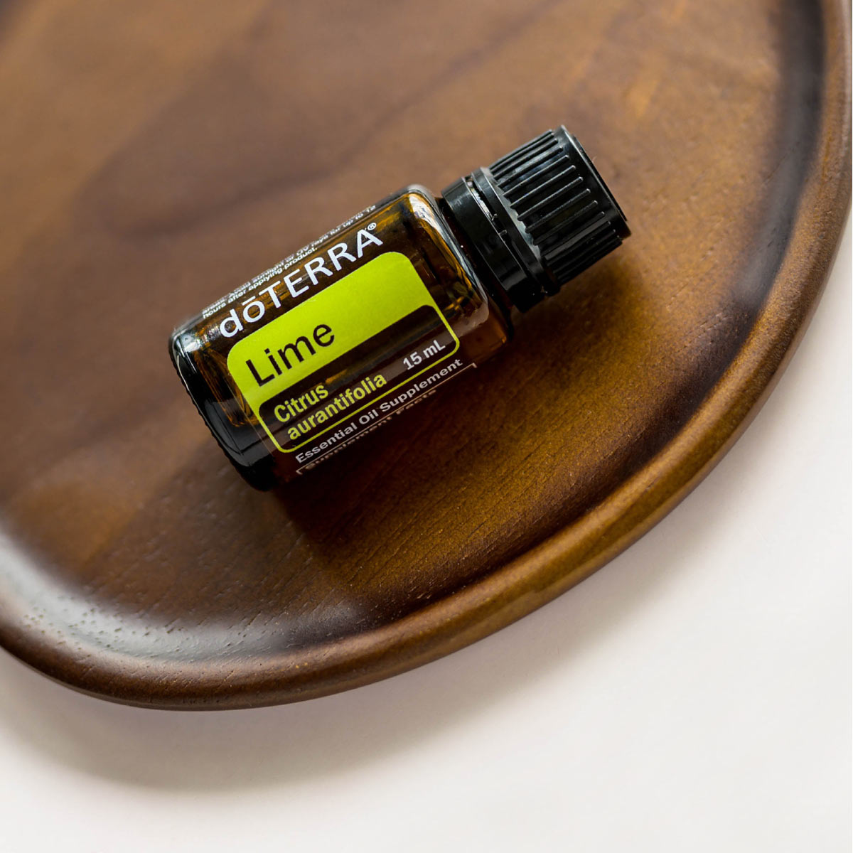 Lime essential oil bottle resting on a wooden dish. What are the top uses for Lime oil? Lime essential oil is commonly used for cooking, cleaning skincare, to promote an uplifting mood, and internal benefits.