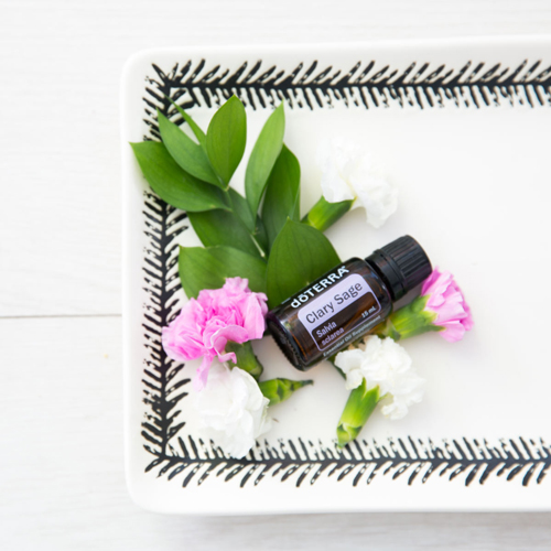 Decorative plate, bottle of clary sage oil, green leaves, pink and white flowers. Keep reading to learn everything you need to know about how to use clary sage essential oil.
