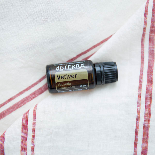 Vetiver essential oil bottle, dish towel with red stripes. Where do you apply vetiver essential oil? Vetiver oil can be applied to the skin, used internally, and added to an essential oil diffuser to be used aromatically.