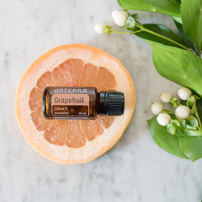 A bottle of doTERRA Grapefruit oil and a slice of grapefruit. Grapefruit is a cleansing, uplifting oil that has a wide variety of benefits for the body, skin, and emotions.
