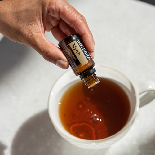 Bottle of Myrrh essential oil, oil droplets being poured into a cup of tea. You can use Myrrh oil for healthy looking skin, mouth and teeth, and for internal benefits.