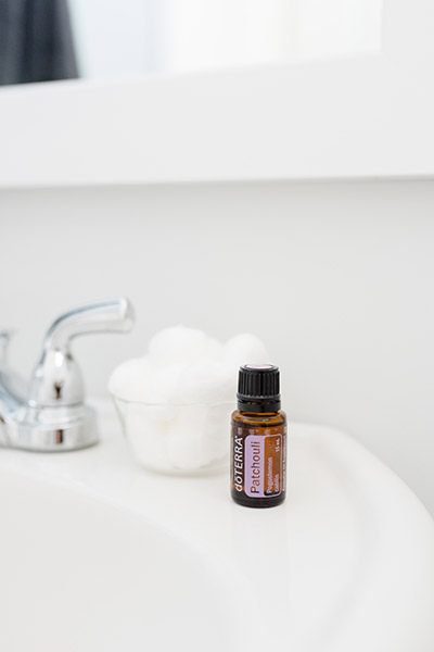 doTERRA Patchouli essential oil sitting on a white sink next to a faucet and a bowl of cotton balls.