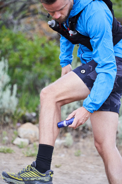 A man with his foot rested on a rock rubbing doTERRA Deep Blue Rub on his calf before he begins his trail run.