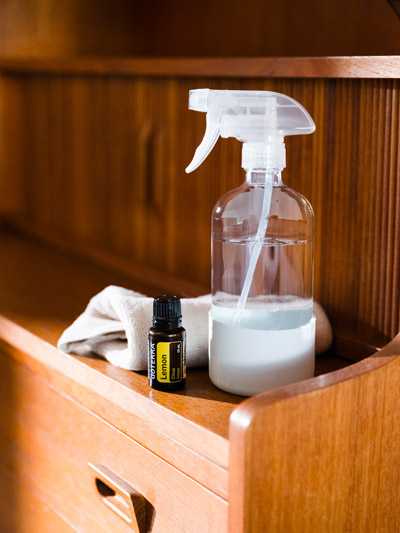 doTERRA Lemon essential oil sitting on a brown, wooden shelf. A glass spray bottle and cloth sit beside it. 