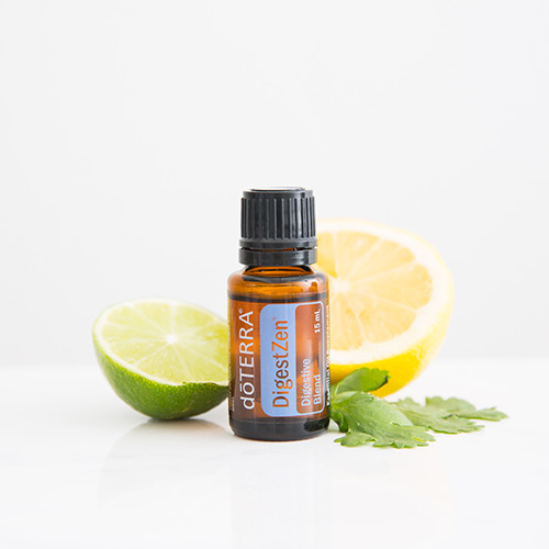 doTERRA DigestZen blend sitting on a white surface with half of a lemon, half of a lime, and leaves behind the bottle.