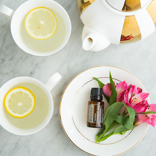 Copaiba laying on a white plate with flowers beside it. A pot with cups of tea surrounding it.