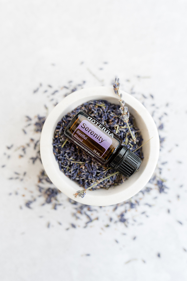 A bottle of doTERRA Serenity Restful Complex oil resting in a bowl filled with fresh sprigs of lavender, creating a calming and soothing visual that highlights the product’s relaxing qualities.