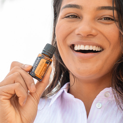 A smiling woman holding a bottle of doTERRA Citrus Bliss essential oil.