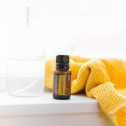 A bottle of Lemon Essential Oil next to a yellow washcloth and a clear glass