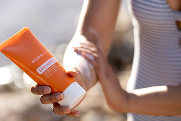 A woman applying doTERRA sun Face and Body Lotion onto her forearm by the beach.