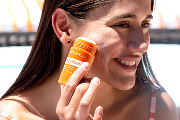Woman smiling while holding a doTERRA sun Face and Body Stick beside her face.