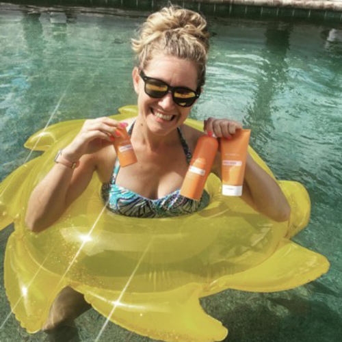 Woman in a pool smiling and holding doTERRA sun products