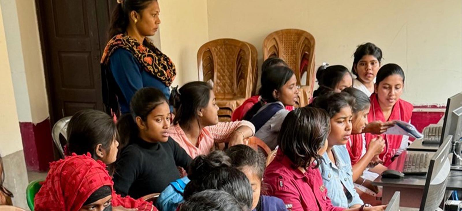 A group of women attentively watching a laptop presentation, led by another woman in a classroom setting.