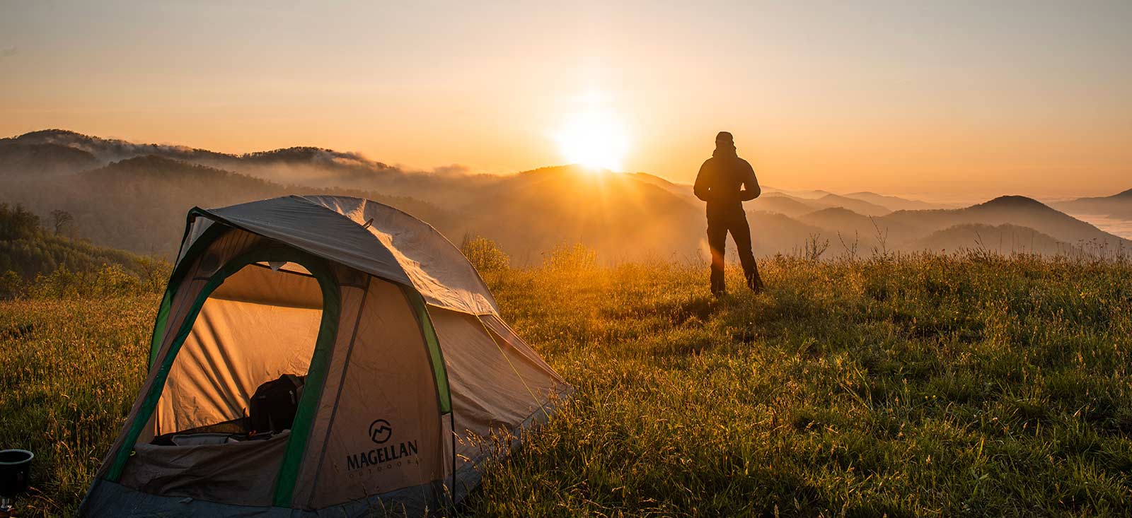 Man out of a tent looking to the sunrise