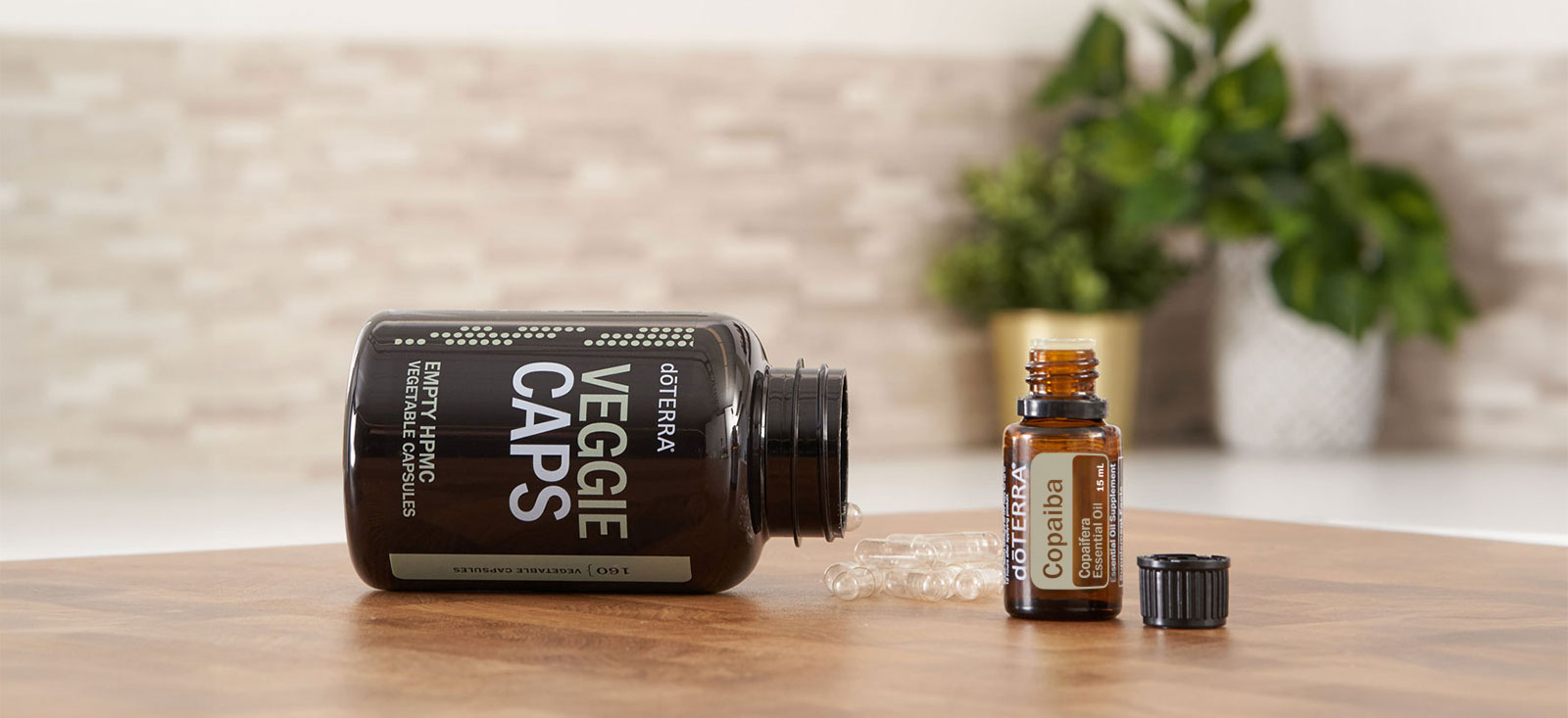 Bottle of doTERRA Veggie caps and a Copaiba essential oil on a wooden table, with a blurred plant and tiled wall in the background.