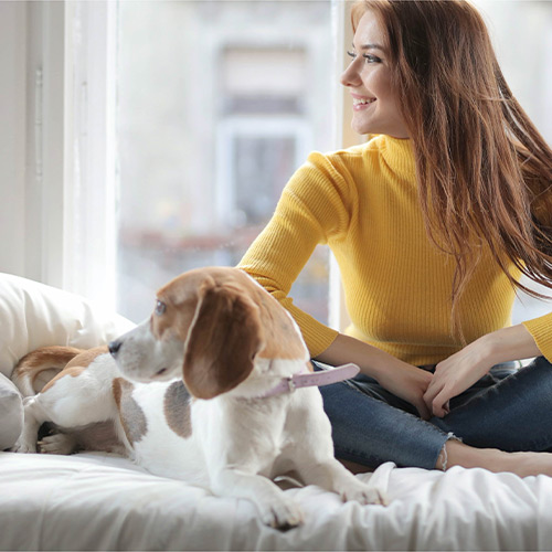 A woman sitting on a bed with her dog.