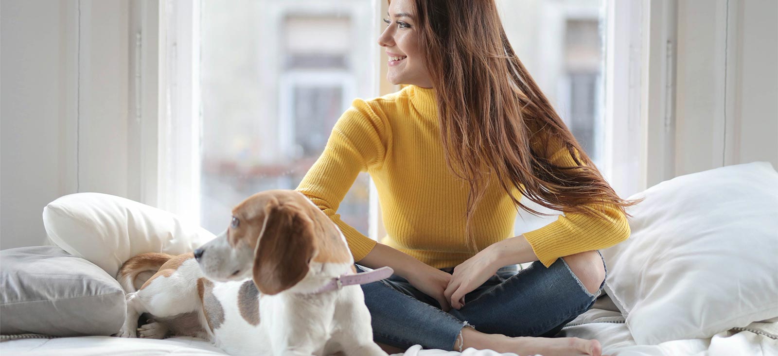 A woman sitting on a bed with her dog.