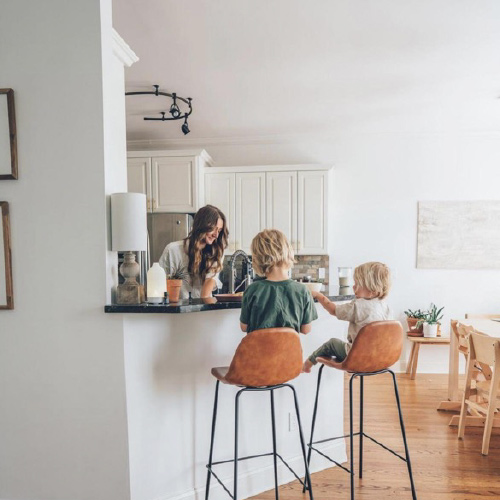 A mother is standing in the kitchen with her sons sitting on chairs