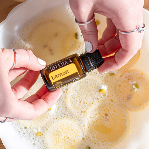 A person adding doTERRA's Lemon Essential Oil to a bowl of water and floating lemons.