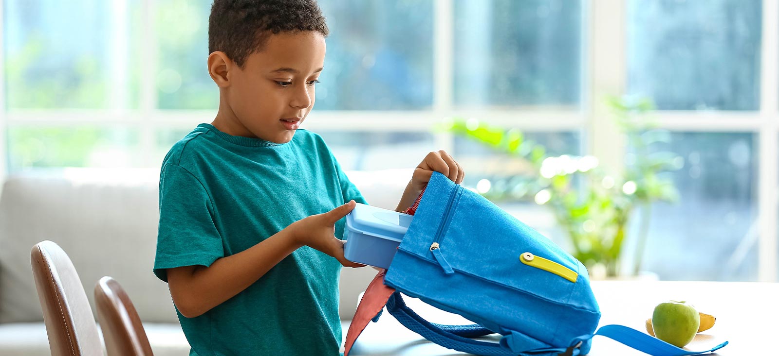 Boy putting lunchbox inside backpack