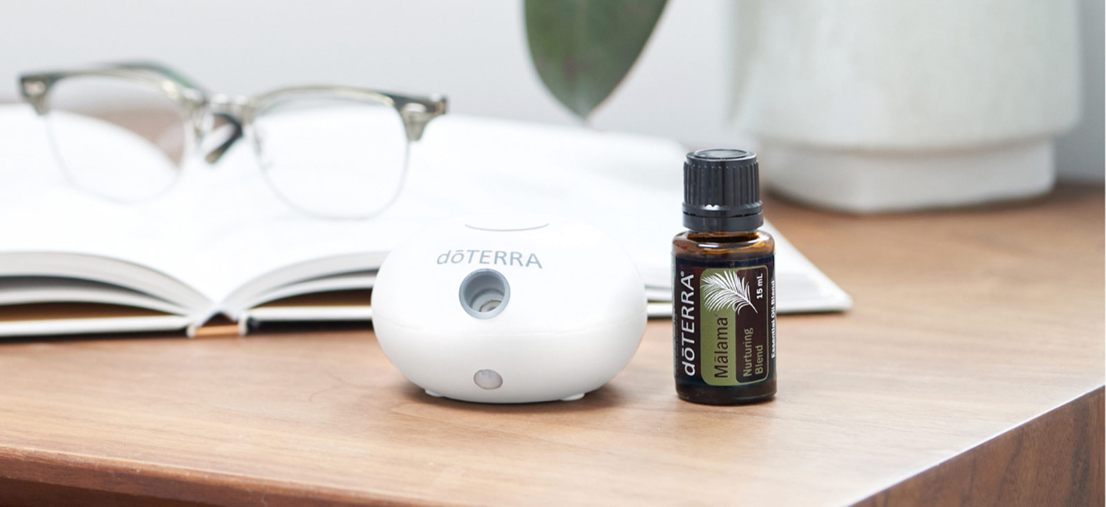 A bottle of doTERRA Malama essential oil sits on a table next to a book