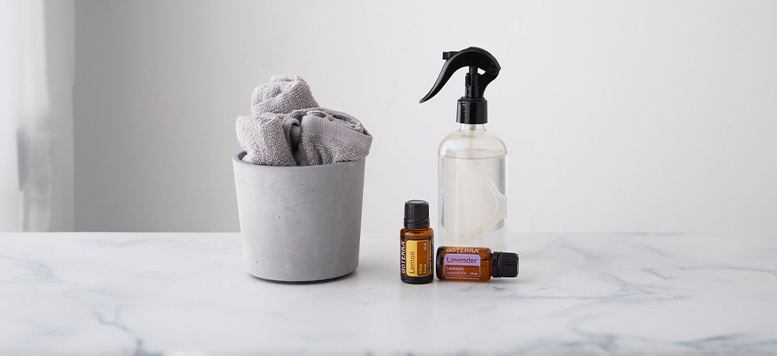 A cloth in a gray concrete pot beside a clear spray bottle and two doTERRA Essential Oils bottles on a marble surface