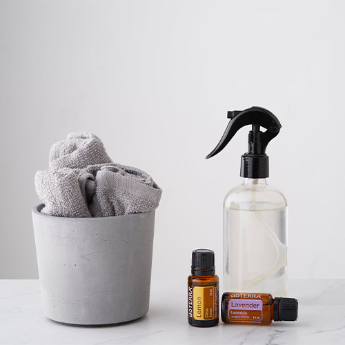 A cloth in a gray concrete pot beside a clear spray bottle and two doTERRA Essential Oils bottles on a marble surface