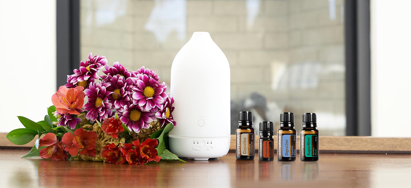 Laluz diffuser and doTERRA essential oils are placed on a table near a vase of flowers.