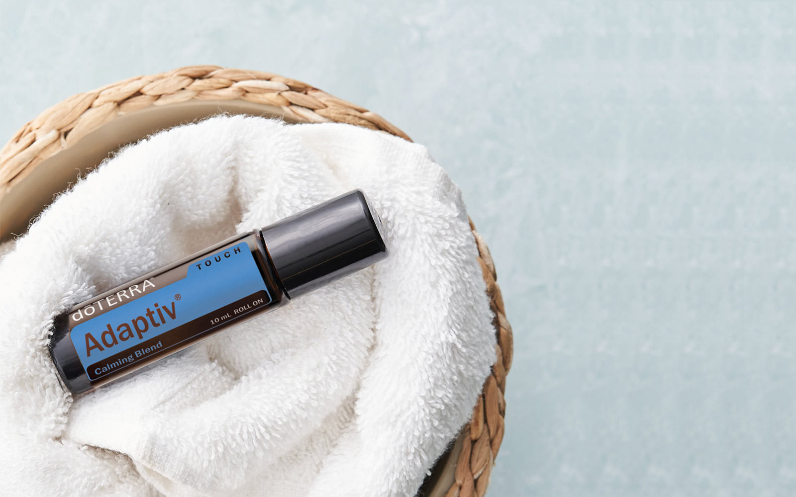 doTERRA Adaptiv Touch roll-on bottle on a white towel in a woven basket with a light blue background.