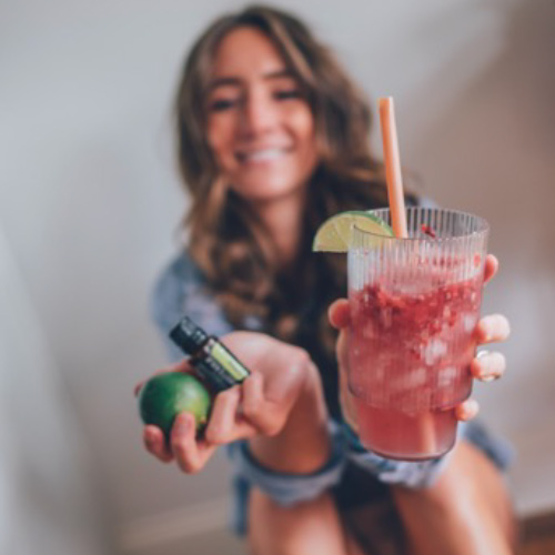 Woman holding lime essential oil and cup of raspberry limeade