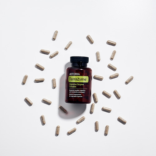 Bottle of doTERRA Terrazyme digestive enzymes surrounded by scattered capsules on a white background.