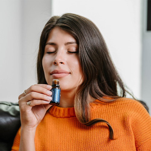 A woman holding a bottle of Adaptiv essential oil while sitting on a couch.