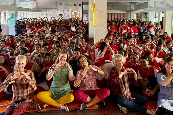 Group of women and students in red uniforms forming heart shapes with their hands in a school hall.