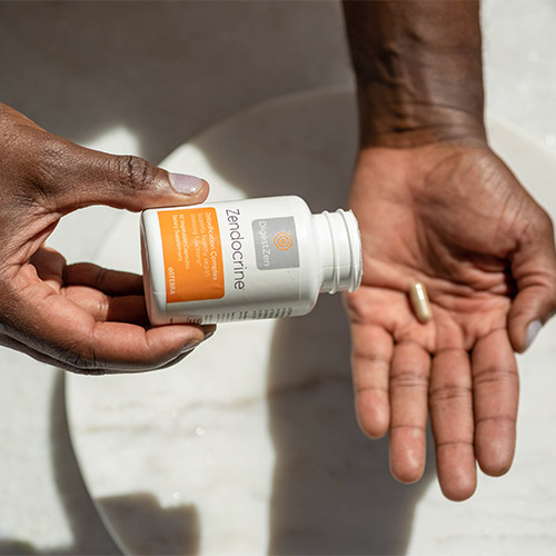 Person holding a doTERRA Zendocrine Complex bottle while dispensing a capsule into their hand.