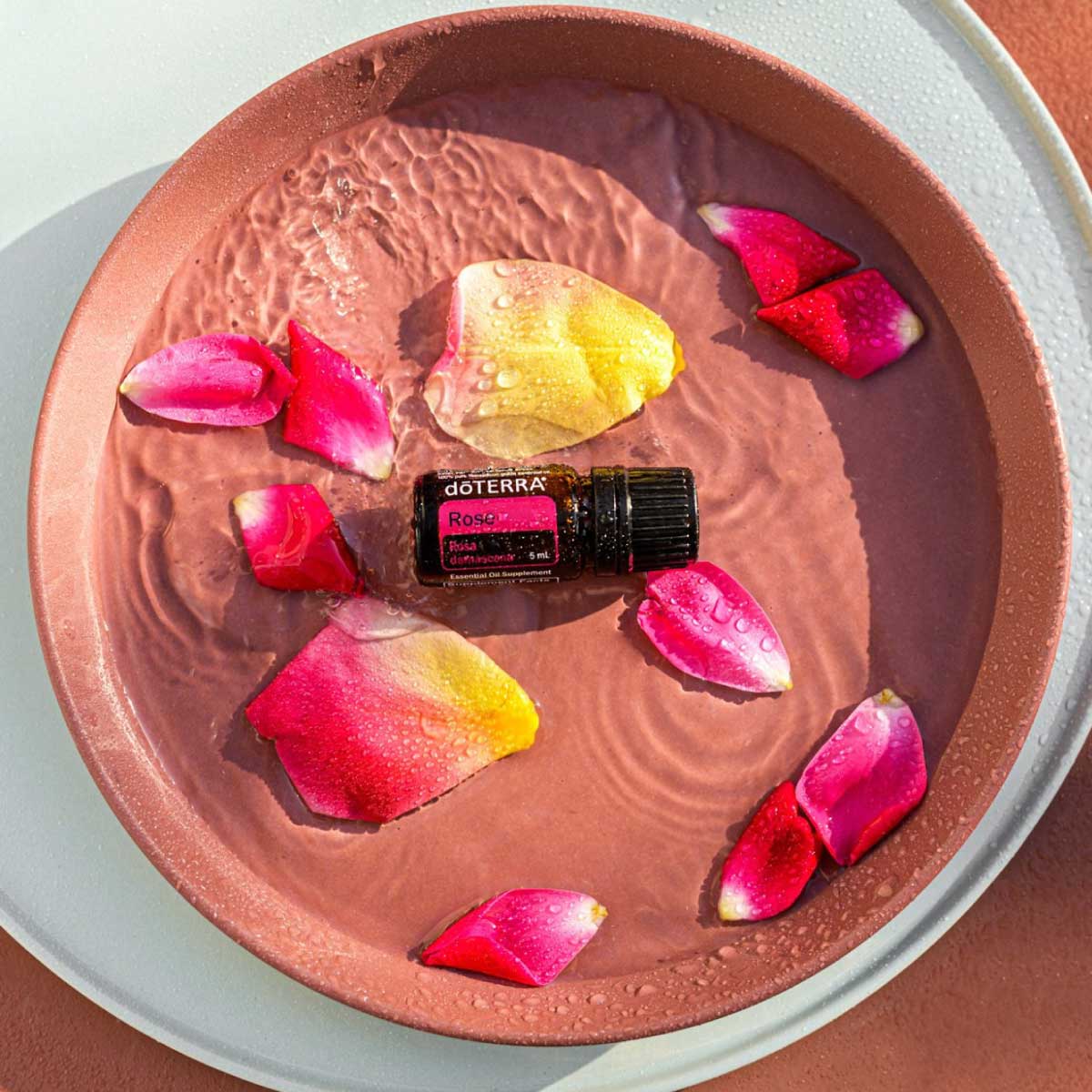 Bottle of Rose essential oil in a dish of water, surrounded by fresh rose petals. What are the benefits of Rose oil? Rose essential oil has benefits for the skin and has long been revered for its uplifting aroma.